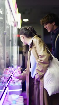 Young friends are having a joyful time playing a claw machine at an arcade in the city. Their smiles and playful interactions highlight the fun and excitement of urban entertainment.