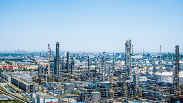 Industrial chemical plant with complex steel pipelines and storage tanks under a clear blue sky.