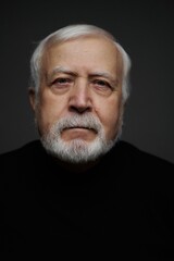Fototapeta premium Older man with white beard looks directly at the camera in a dark setting