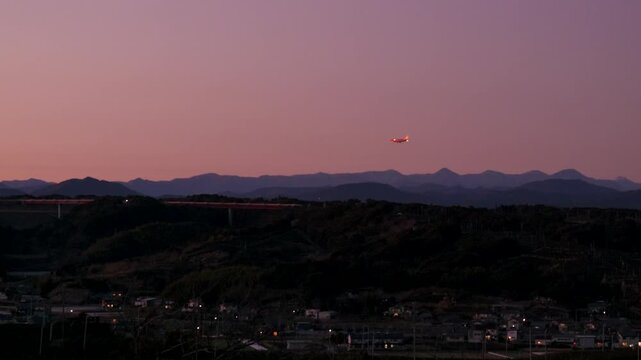 夕暮れの空を着陸するジェット機と遠くの山並み、誘導灯が輝く日本の風景
