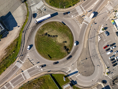 Aerial view of cars and a bus navigating the roundabout's circular dance, amidst the crisp lines of pedestrian crossings, Albergaria-a-Velha, Portugal.