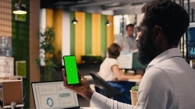 Vertical green screen, smartphone, black employee, working in office, research and development, global business, corporate lifestyle. Business intel, task management, monetary data.