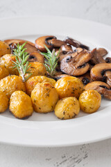 Roasted baby potatoes with sauteed mushrooms and rosemary on minimalist white plate