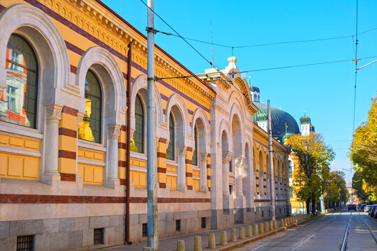 Central Sofia Market Hall in Bulgaria with Neo Renaissance facade with yellow and red brick detailing. Arched windows and historic architecture along street with tram tracks, near Banya Bashi Mosque