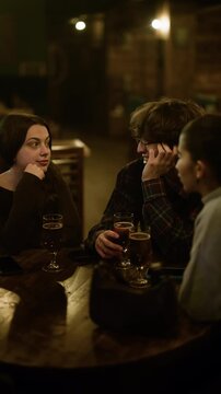 Young friends are deeply engaged in conversation, sharing drinks at a cozy bar in the city. Their relaxed smiles and gestures highlight a warm social gathering filled with enjoyment and connection.