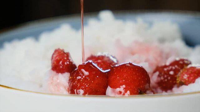 Thick strawberry jam or syrup poured over fresh strawberries with rice garnish. Sweet berry dessert with jam, food presentation and confectionery concept.