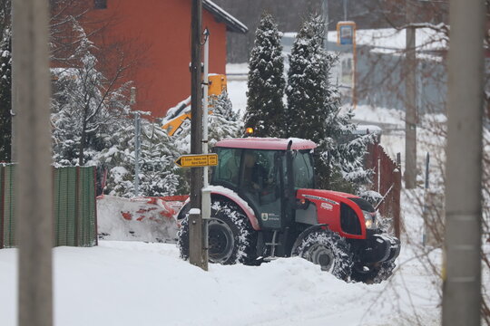Red Zetor tractor parked on snowy street near residential houses during winter maintenance