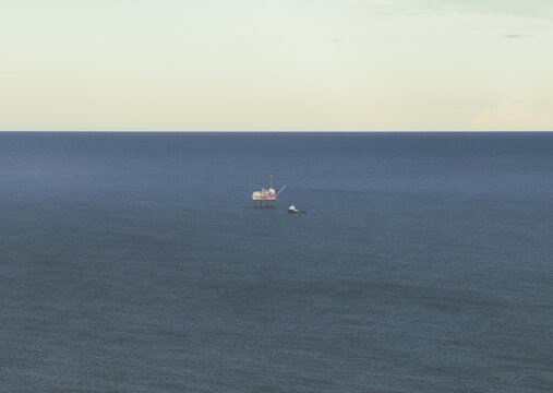 Aerial view of an offshore oil rig stands prominently in the vast expanse of the deep blue sea, under a pale sky, San Juan de Gaztelugatxe, Euskadi, Spain.