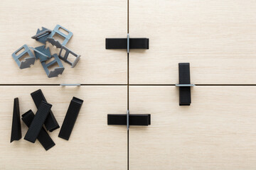 Plastic gray clips and black wedges for floor or wall tiles surface leveling. Beige ceramic tiles gluing. Closeup. Renovation process. Repair work of home. Top down view.