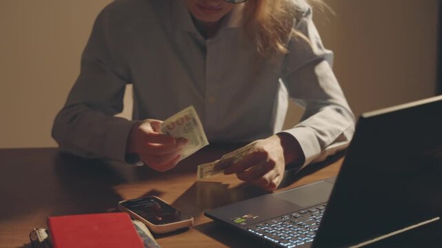 unhappy tired woman working on laptop overloaded with work, sitting at desk in office overtime job. Sad face girl in stress anxiety lack of money. Person counting money few dollars bills, small salary