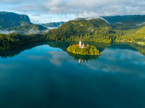 Aerial view of the iconic Bled Island, crowned with the Church of the Assumption, reflects serenely on the tranquil lake under a soft, diffused light, Bled, Radovljica, Slovenia.