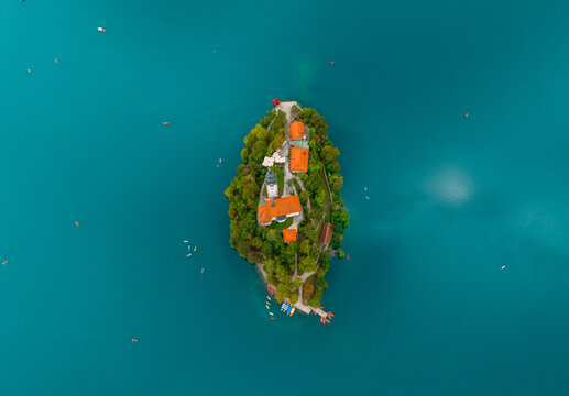 Aerial view of Bled Island's terracotta roofs and lush greenery amidst the serene turquoise waters of Lake Bled, Radovljica, Slovenia.