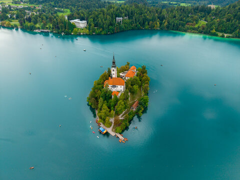 Aerial view of the iconic Church of Mary the Queen on Bled Island, standing serene amidst the turquoise waters of Lake Bled, surrounded by lush green forests, Bled, Radovljica, Slovenia.