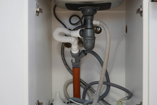 Under sink plumbing pipes and drainage system inside kitchen cabinet