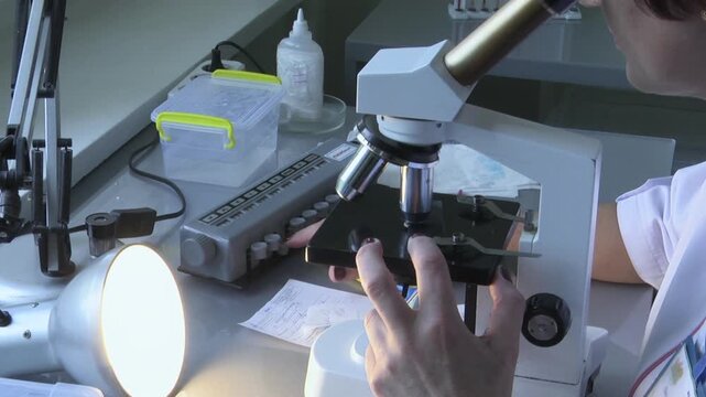 Scientist adjusting the stage of a professional compound microscope during detailed lab analysis under bright, controlled lighting.