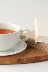 Fototapeta premium Hot tea in a white cup on a wooden board with napkins nearby in a simple setting