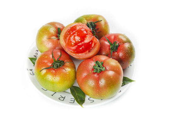 Fresh Ripe Heirloom Tomatoes with Water Droplets on White Plate, One Sliced Open Showing Red Interior