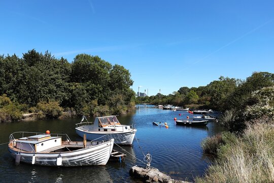 Motorboats on a canal in Copenhagen's Christiania district. In the distance, the Amager Bakke industrial building, also known as CopenHill, a waste-to-energy plant, is visible.