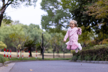 Naklejka premium Young girl joyfully jumping on a park path surrounded by trees
