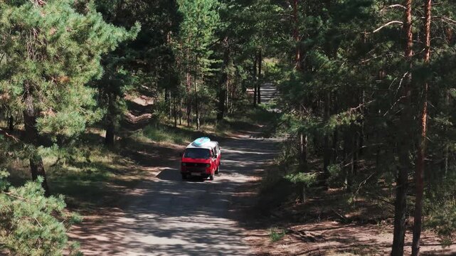 Red camper van driving forest road with surfboard