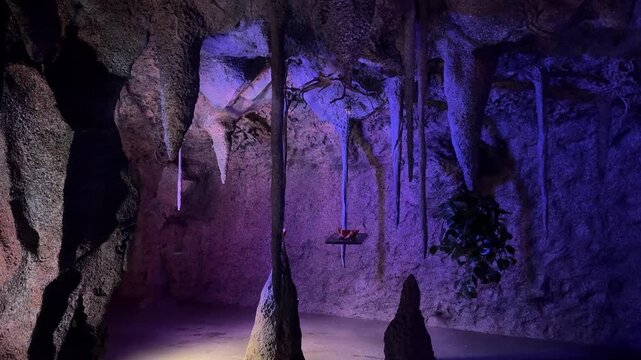 Bats in flight inside a limestone cave with stalactites and stalagmites, lit by blue purple light. Underground wildlife scene for nature, geology, adventure, spooky travel and conservation.