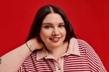 Fototapeta premium Stylish plus size woman showcasing confidence against a vibrant red backdrop with charm