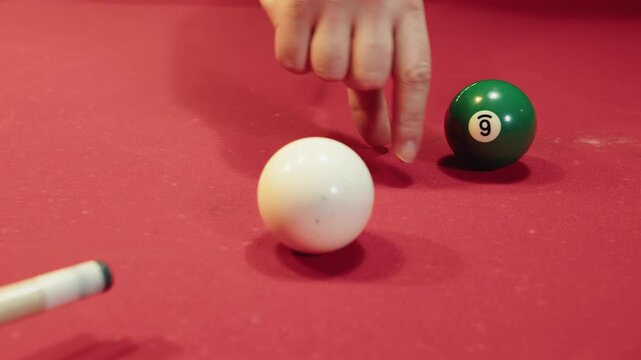 The trainer's fingers tell how to do shot beside green object ball on red felt table, close up shows players fingers forming stable bridge near cue ball, billiards aim and cue alignment in pool hall