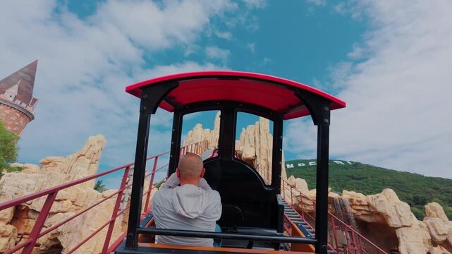 Riding the roller coaster up the track at the amusement park on a bright day with clouds in the sky