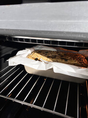 Freshly baked whole grain bread with seeds in a parchment-lined loaf pan inside an oven, showcasing golden crust and warm lighting. Gluten-free home baking concept, green buckwheat bread