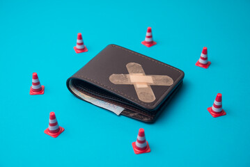 Traffic cones surrounds the injured leather wallet with little money cash on blue background. Personal broke financial problem, bankruptcy, over burden, poor, social issues and so on concept.