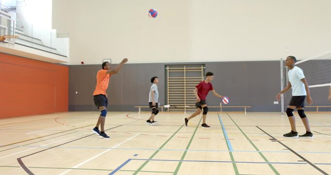 Diverse male teammates responding to setter tossing volleyball bumping passing during gym drill