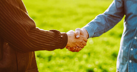 Two people shake hands in a green field during the day. This scene captures a moment of agreement...