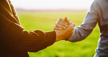 Two people shake hands in a green field during the day. This scene captures a moment of agreement...