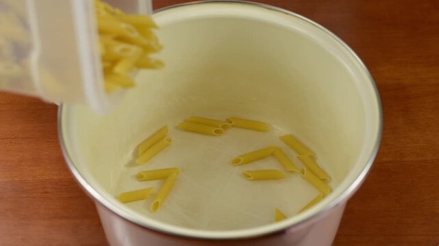 Pouring dry macaroni pasta into a metal pot with sound