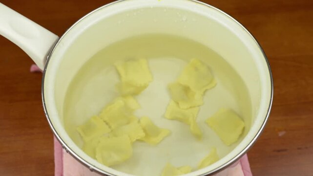 Dropping fresh tortellini pasta one by one into a pot of water with water splashing with sound
