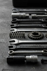 Fototapeta premium A collection of various metal tools including wrenches, sockets, a gear, and a spring, arranged on a textured dark surface.