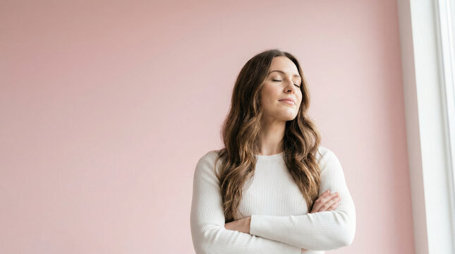 A happy modern woman finds inner peace and mental health while relaxing against a pink wall with her eyes closed.