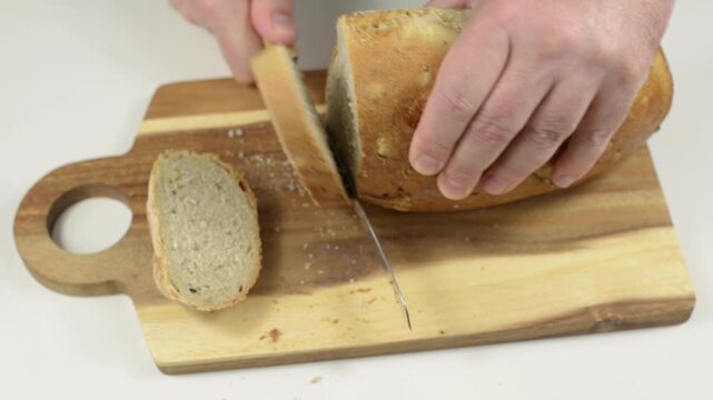 Slicing fresh dark bread with a serrated bread knife on a wooden board with sound