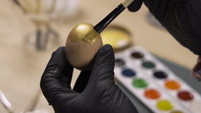 Female hands coloring eggs with golden paint, close-up. Easter, traditions, holidays and people
