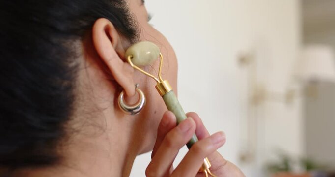 Woman is bringing jade roller to jaw by ear and rolling upward, reducing puffiness at vanity