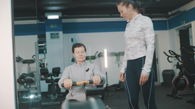 Personal trainer coaching senior woman on rowing machine