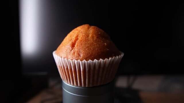 A close-up shot of a golden-brown muffin in a white paper wrapper, highlighting its perfectly domed top and slightly crisp texture. 