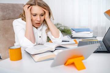 Stressed woman student holding head in hands near books and laptop, tired adult teacher feeling...