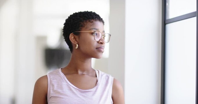 African American woman standing near large window, turning toward camera noticing lens and smiling