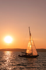 Fototapeta premium Sailing boas floating gently on the calm water at sunset near the coast in summer, setting sun beach landscape, goldenorange lights, calm and serenity
