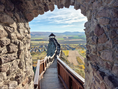 Scenic view of the famous wooden walkway of Boldogko Castle in Hungary through a stone arch, overlooking the autumn landscape of the Zemplen Mountains, castles and medieval theme