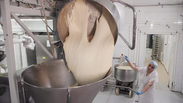 Worker pouring a large dough batch from a kettle in an industrial bakery.