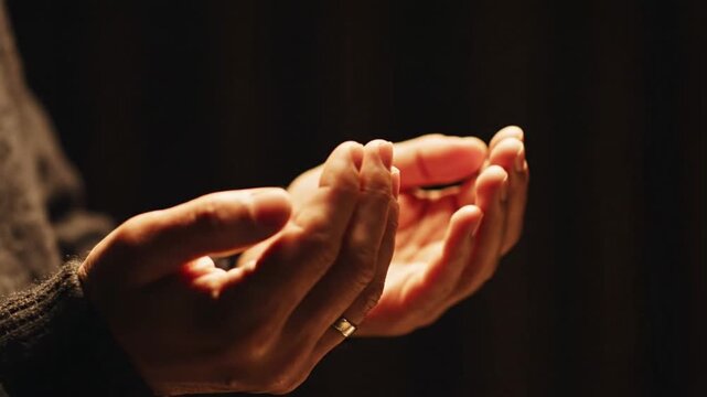 Hands cupped in a dark setting with a wedding ring visible