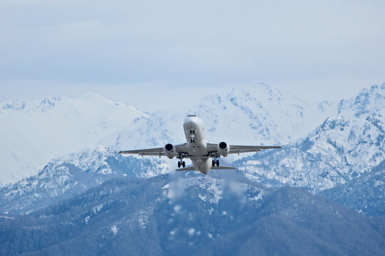 White Airplane Taking Off Against Snowy Mountains in Cloudy Weather