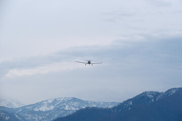 Light single-engine airplane climbing over snow-capped mountains in cloudy weather